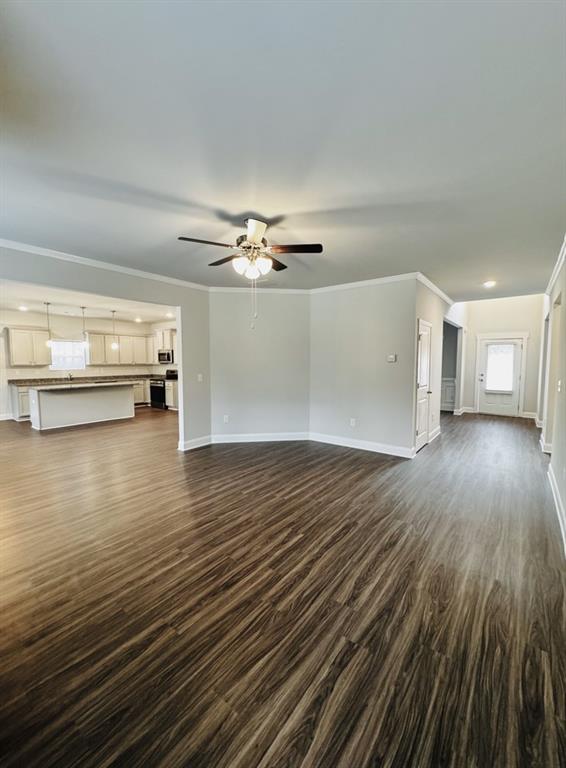 unfurnished living room featuring crown molding, dark wood finished floors, ceiling fan, and baseboards