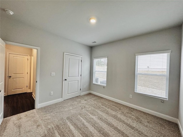unfurnished bedroom featuring baseboards, dark carpet, and visible vents