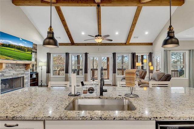 kitchen featuring light stone counters, a fireplace, sink, decorative light fixtures, and white cabinets