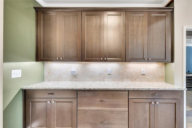 kitchen with backsplash, light stone counters, and crown molding