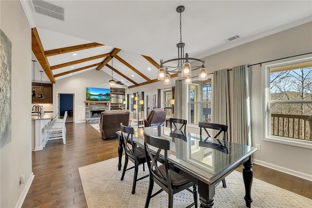 dining area featuring ceiling fan with notable chandelier, dark hardwood / wood-style flooring, lofted ceiling with beams, and a stone fireplace