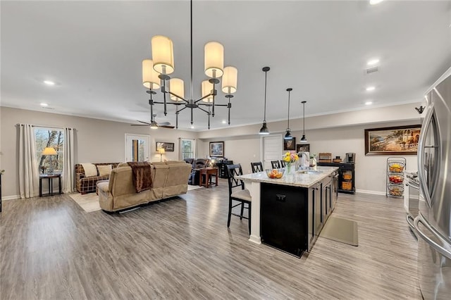 kitchen featuring light stone counters, pendant lighting, light hardwood / wood-style floors, a kitchen island, and ceiling fan with notable chandelier