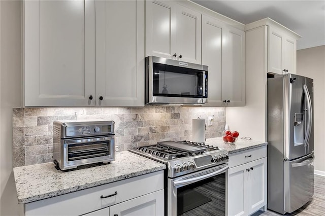 kitchen with white cabinets, light stone counters, backsplash, and appliances with stainless steel finishes