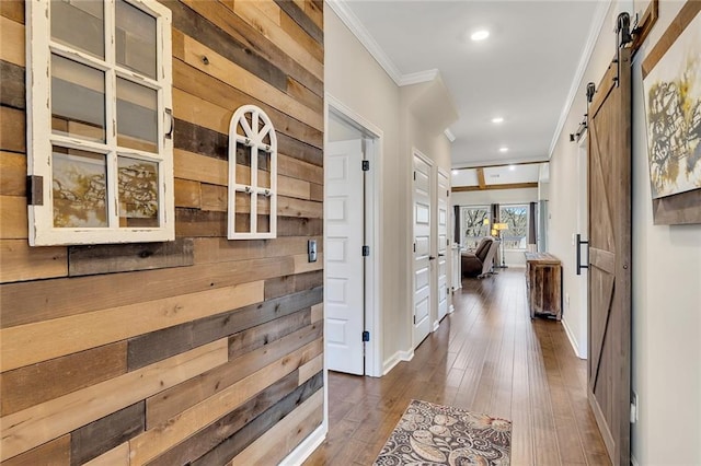 hall with a barn door, wood walls, crown molding, and dark hardwood / wood-style flooring