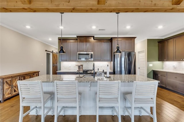 kitchen with appliances with stainless steel finishes, a barn door, decorative light fixtures, and a kitchen island with sink