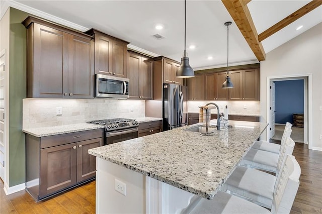 kitchen with appliances with stainless steel finishes, a center island with sink, light stone counters, and hanging light fixtures