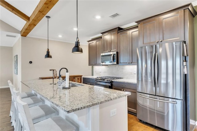 kitchen with pendant lighting, stainless steel appliances, a kitchen island with sink, and sink