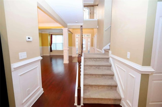 stairs with ornate columns, a decorative wall, wood finished floors, and wainscoting