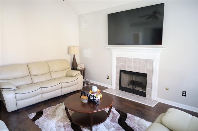 living room with dark hardwood / wood-style floors, vaulted ceiling, ceiling fan, and a tiled fireplace