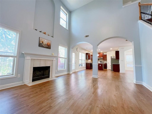 unfurnished living room with a tiled fireplace, light hardwood / wood-style flooring, and a towering ceiling