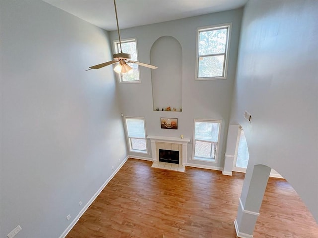 unfurnished living room featuring a tile fireplace, hardwood / wood-style floors, plenty of natural light, and ceiling fan