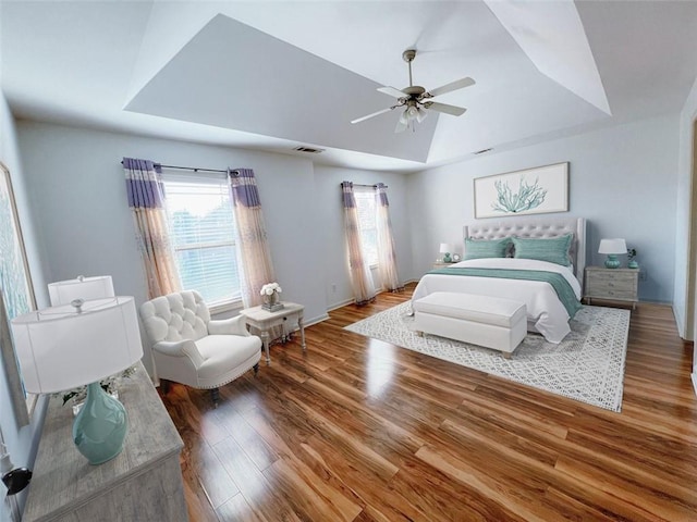 bedroom featuring ceiling fan, wood-type flooring, and a tray ceiling