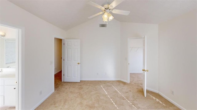 unfurnished bedroom with ensuite bath, ceiling fan, a spacious closet, vaulted ceiling, and light colored carpet