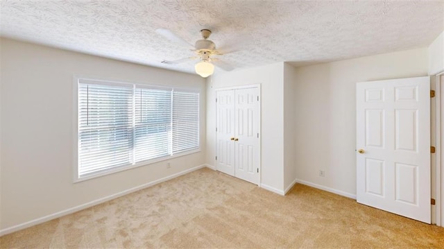 unfurnished bedroom featuring a textured ceiling, light colored carpet, a closet, and ceiling fan