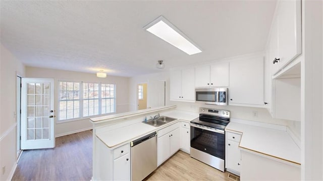 kitchen with sink, stainless steel appliances, white cabinets, kitchen peninsula, and light wood-type flooring