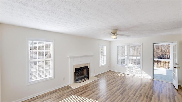 unfurnished living room featuring ceiling fan, wood-type flooring, a tile fireplace, and a textured ceiling