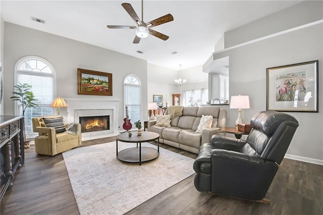 living room with dark hardwood / wood-style flooring, ceiling fan with notable chandelier, high vaulted ceiling, and a premium fireplace