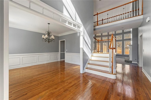 staircase with hardwood / wood-style flooring, ornamental molding, a high ceiling, and a chandelier