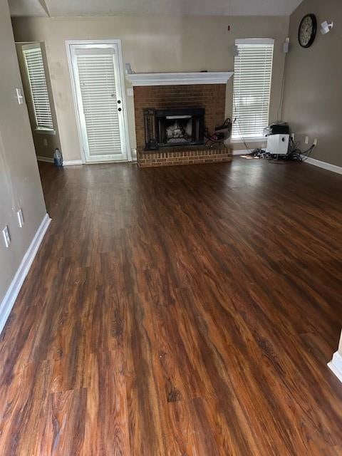 unfurnished living room featuring a brick fireplace and dark hardwood / wood-style flooring