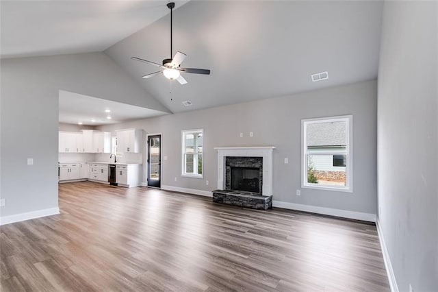 unfurnished living room featuring ceiling fan, sink, hardwood / wood-style flooring, high vaulted ceiling, and a stone fireplace