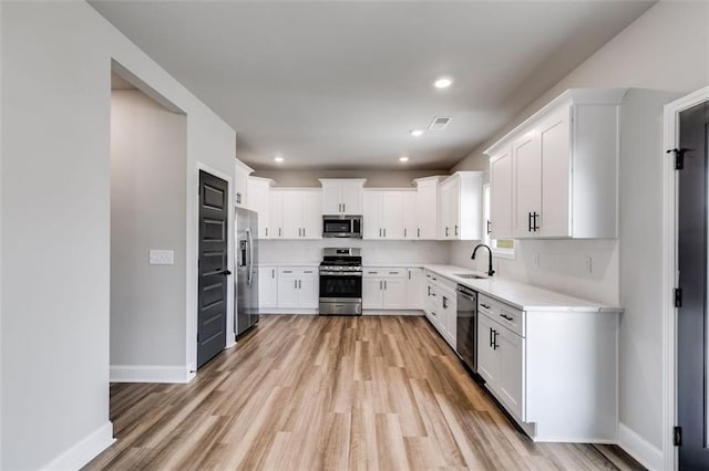 kitchen with sink, white cabinets, stainless steel appliances, and light hardwood / wood-style flooring