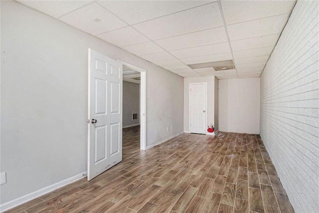 empty room featuring hardwood / wood-style flooring, a drop ceiling, and brick wall