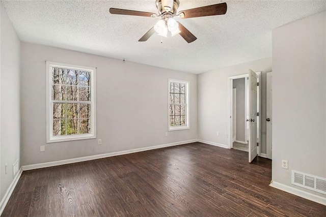 empty room with a textured ceiling, plenty of natural light, dark wood-type flooring, and ceiling fan