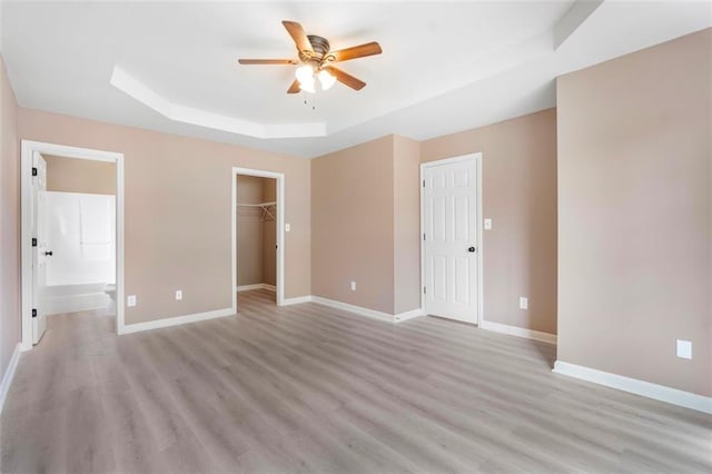 unfurnished bedroom featuring baseboards, a raised ceiling, ensuite bath, and light wood-type flooring