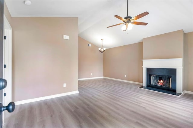 unfurnished living room featuring baseboards, ceiling fan with notable chandelier, a lit fireplace, vaulted ceiling, and wood finished floors