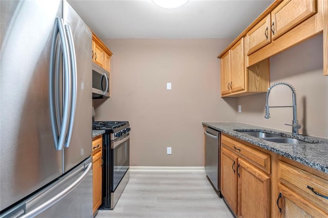 kitchen featuring appliances with stainless steel finishes, baseboards, a sink, dark stone countertops, and light wood-type flooring