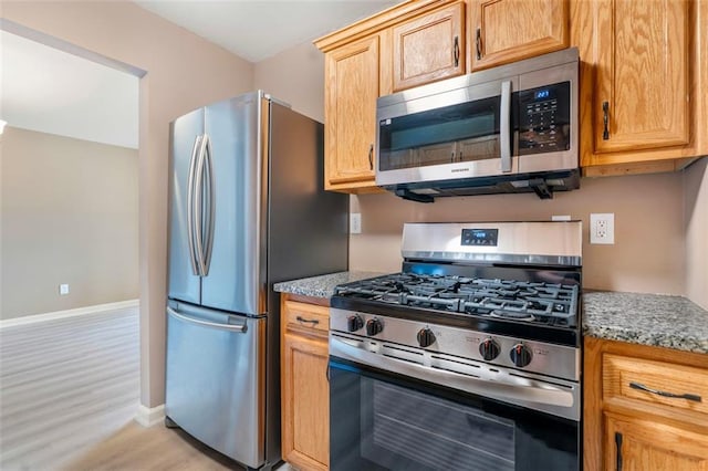 kitchen featuring light stone counters, stainless steel appliances, light wood-style flooring, and baseboards