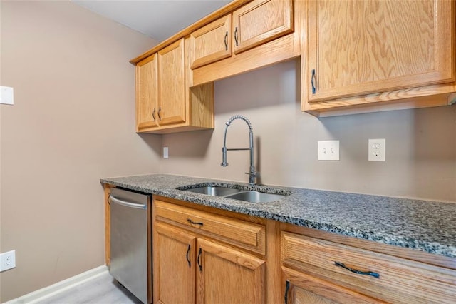 kitchen with dark stone countertops, stainless steel dishwasher, baseboards, and a sink