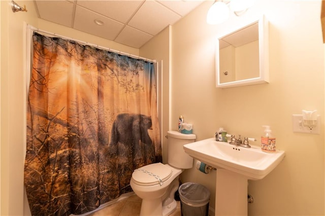 bathroom with a paneled ceiling, curtained shower, sink, tile patterned flooring, and toilet