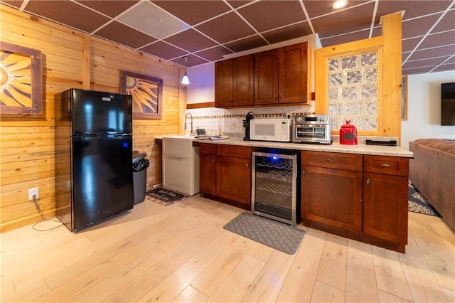 kitchen with black fridge, a paneled ceiling, light wood-type flooring, wooden walls, and beverage cooler