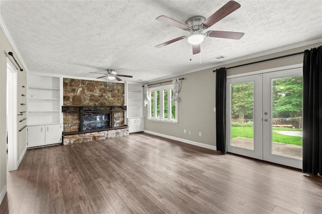 unfurnished living room featuring crown molding, a textured ceiling, dark hardwood / wood-style flooring, a stone fireplace, and french doors