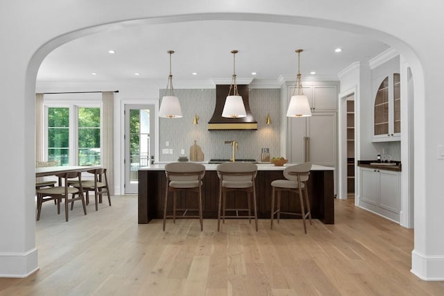 kitchen featuring a center island with sink, pendant lighting, light hardwood / wood-style flooring, and premium range hood