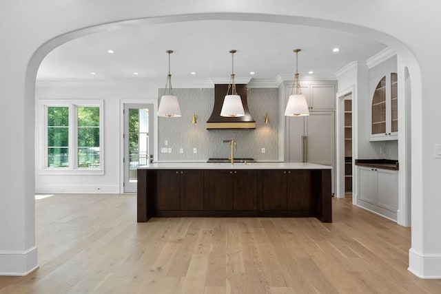 kitchen with light hardwood / wood-style flooring, custom exhaust hood, sink, pendant lighting, and a center island with sink