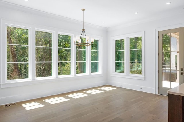 unfurnished dining area featuring wood-type flooring, a chandelier, and crown molding