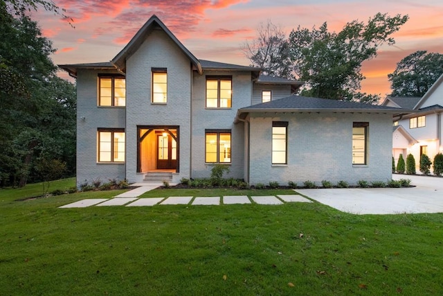 back house at dusk featuring a lawn