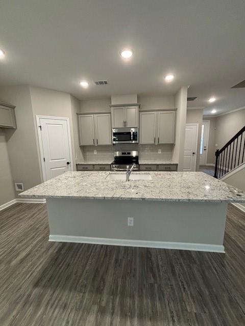 kitchen with light stone counters, an island with sink, gray cabinetry, and stainless steel appliances