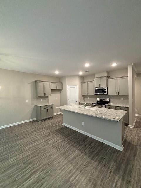 kitchen featuring light stone countertops, appliances with stainless steel finishes, gray cabinets, and a center island with sink