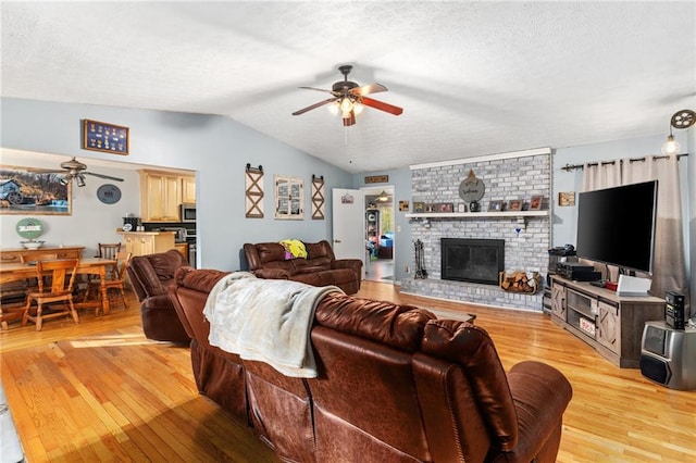 living room with a textured ceiling, ceiling fan, a fireplace, light hardwood / wood-style floors, and lofted ceiling