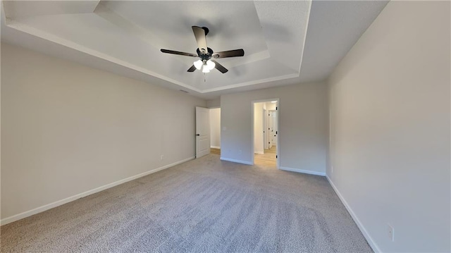 unfurnished bedroom featuring ceiling fan, light colored carpet, and a tray ceiling