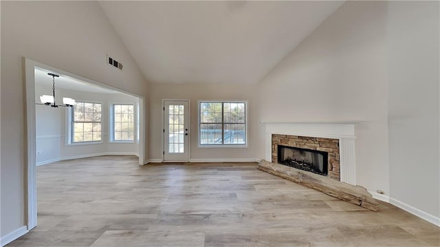 unfurnished living room featuring high vaulted ceiling, an inviting chandelier, light hardwood / wood-style flooring, and a stone fireplace