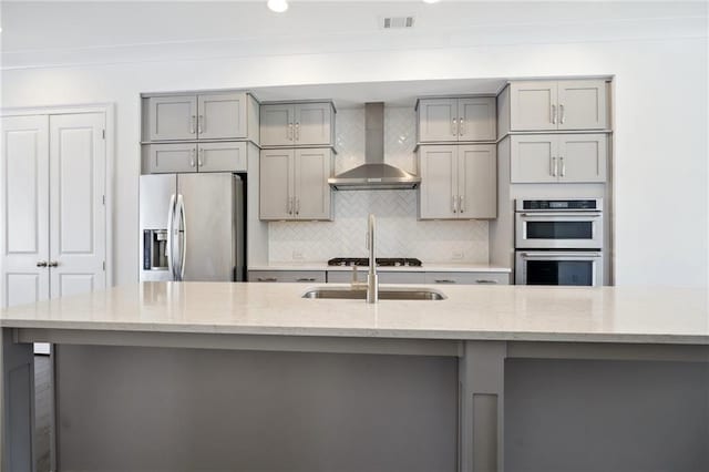 kitchen featuring gray cabinetry, appliances with stainless steel finishes, a spacious island, wall chimney exhaust hood, and light stone counters