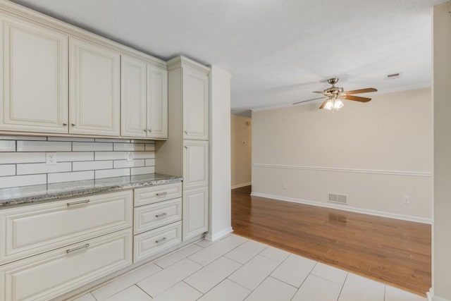 kitchen featuring baseboards, light tile patterned floors, decorative backsplash, light stone counters, and a ceiling fan