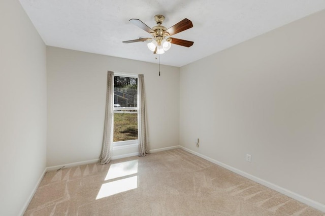 carpeted spare room featuring baseboards and a ceiling fan