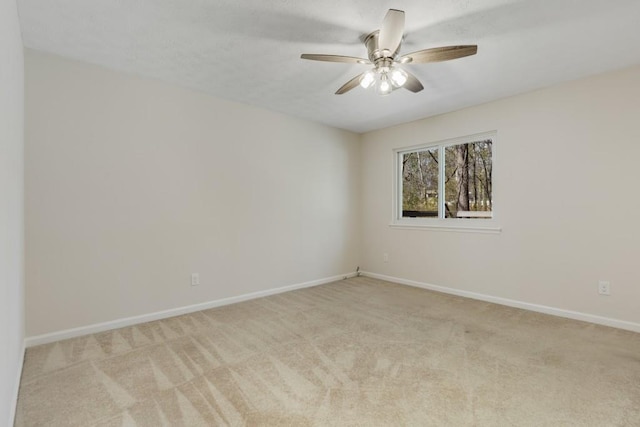 spare room featuring light colored carpet, baseboards, and ceiling fan