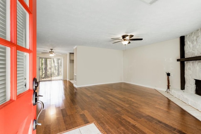 unfurnished living room with a stone fireplace, baseboards, a ceiling fan, and hardwood / wood-style floors