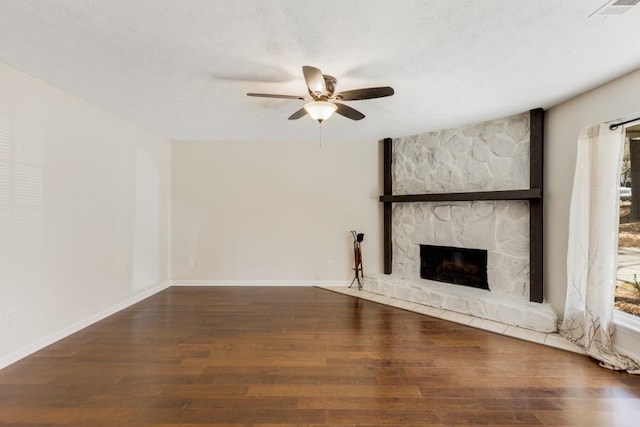 unfurnished living room featuring wood finished floors, visible vents, baseboards, a ceiling fan, and a stone fireplace